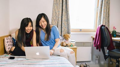 Two students sitting on a bed looking at a laptop