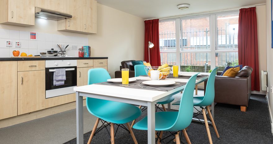 Shared kitchen with a table with chairs, oven, hob and seating are at the background