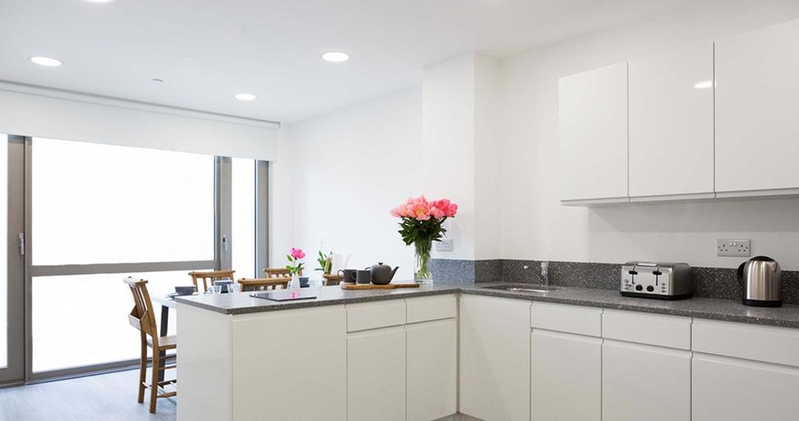 A shared kitchen with cupboards, sink and windows in the background at Chapter Lewisham