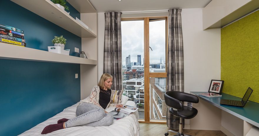 The classic ensuite at Urbanest Hoxton with a study desk, a floor to ceiling window and a student reading on the bed