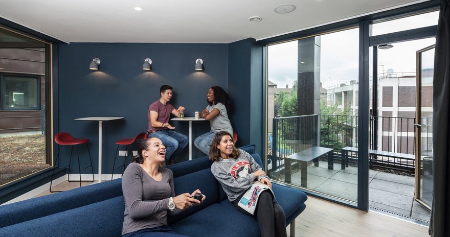 Students in a communal room with sofa, bistro tables and a balcony