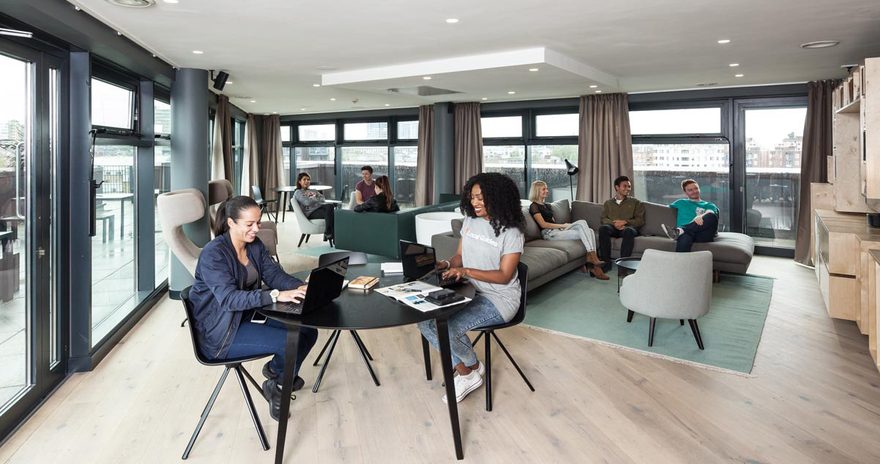 Students in a social space with sofas, armchairs and floor to ceiling windows