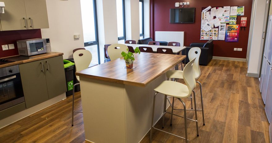 tables and seating area with a TV in the shared kitchen at constantine college