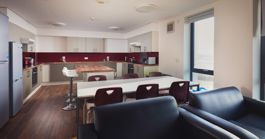 A fully equipped shared kitchen containing armchairs and dining tables at the Constantine College accommodation in York