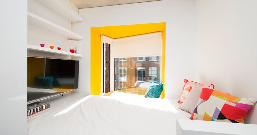 A bed with a TV on the wall and a seating area by the window