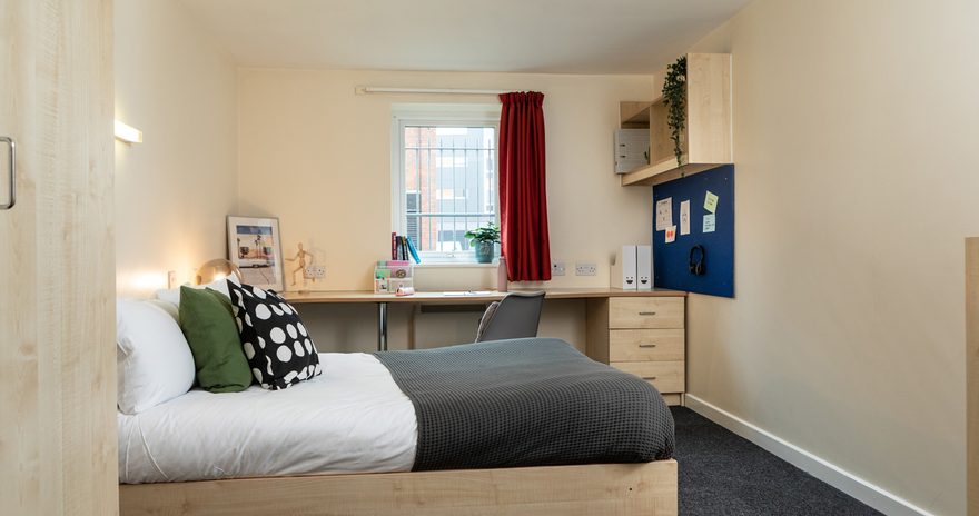 Premium ensuite with a small double bed, wardrobe, study desk, shelves and window
